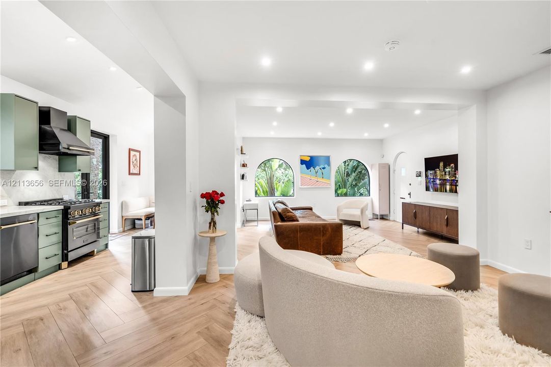 Herringbone wood-finish flooring, recessed lighting, arched windows, matte sage cabinetry, and professional-style range with integrated hood