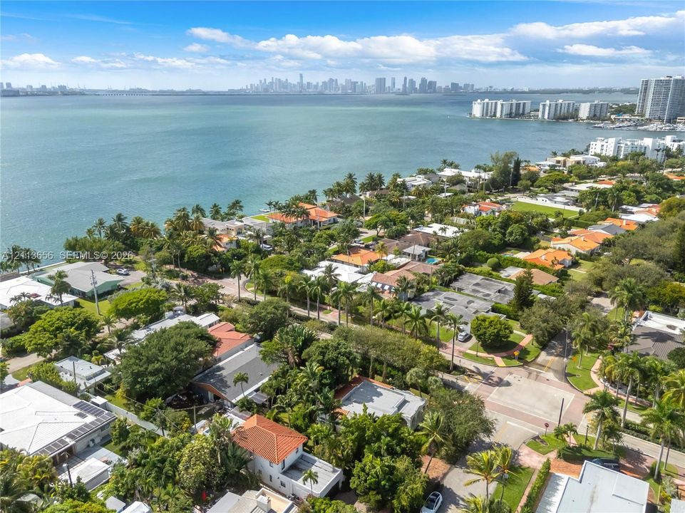 Aerial perspective of coastal residential property featuring expansive waterfront exposure, mature tropical landscaping, and paved street access