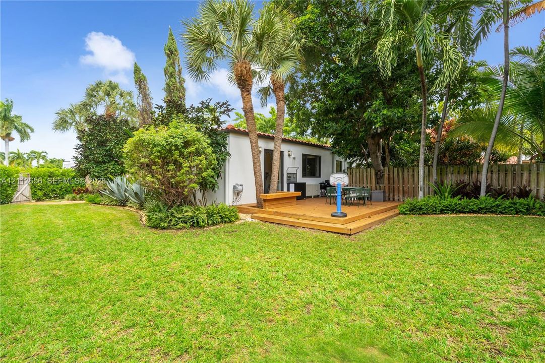 Private backyard featuring a wood-finish deck, mature palm trees, lush landscaping, and perimeter wood fencing