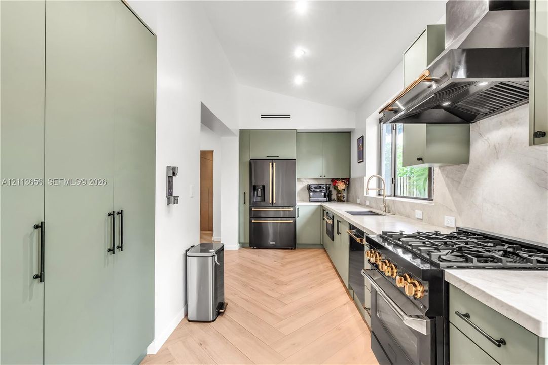 Kitchen featuring sage green flat-panel cabinetry, herringbone-patterned wood-finish flooring, a commercial-style gas range, light-toned stone-finish countertops, and a professional-grade range hood
