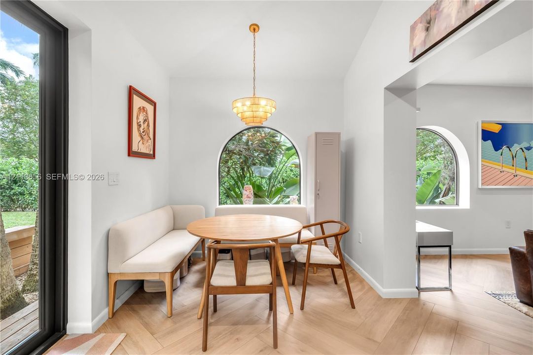 Herringbone wood-finish flooring, vaulted ceilings, multi-tiered brass pendant lighting, and arched windows with exterior greenery