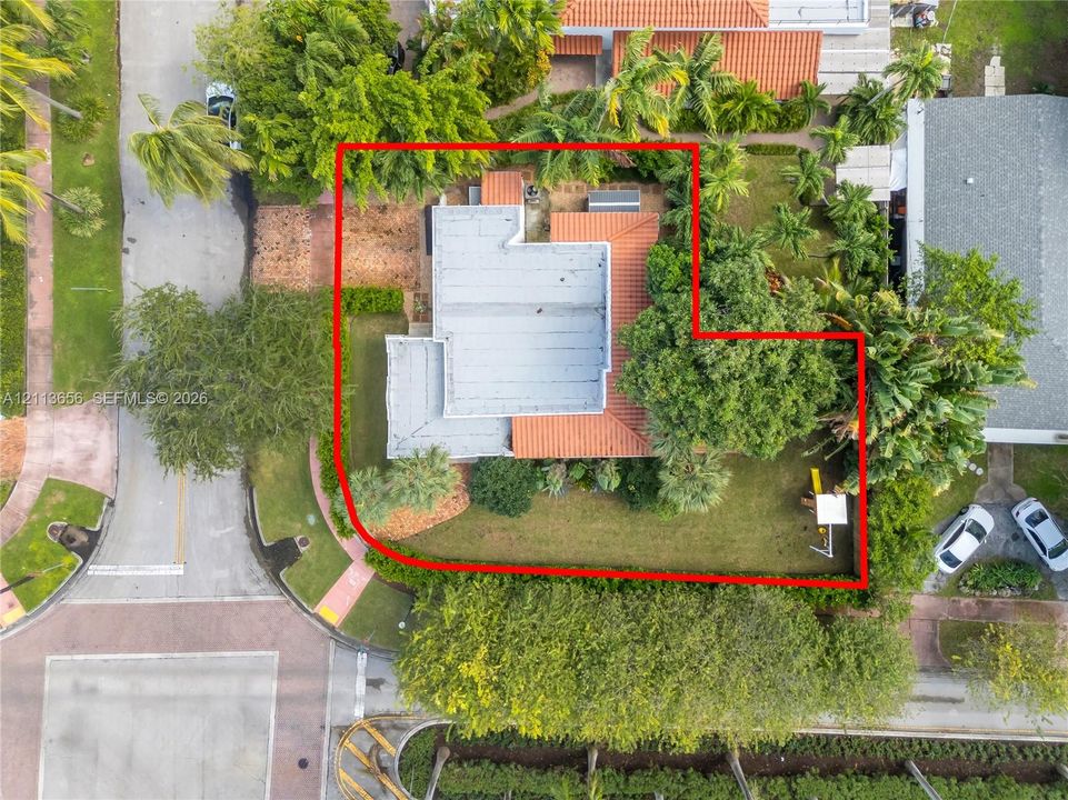 Aerial perspective of corner lot featuring a tile roof, mature palm trees, expansive lawn, and defined property boundaries