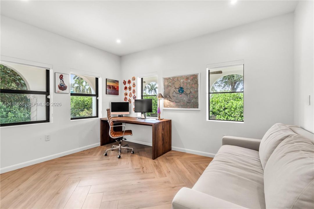 Room featuring wood-finish flooring in a herringbone pattern, three large windows with dark frames, and recessed lighting
