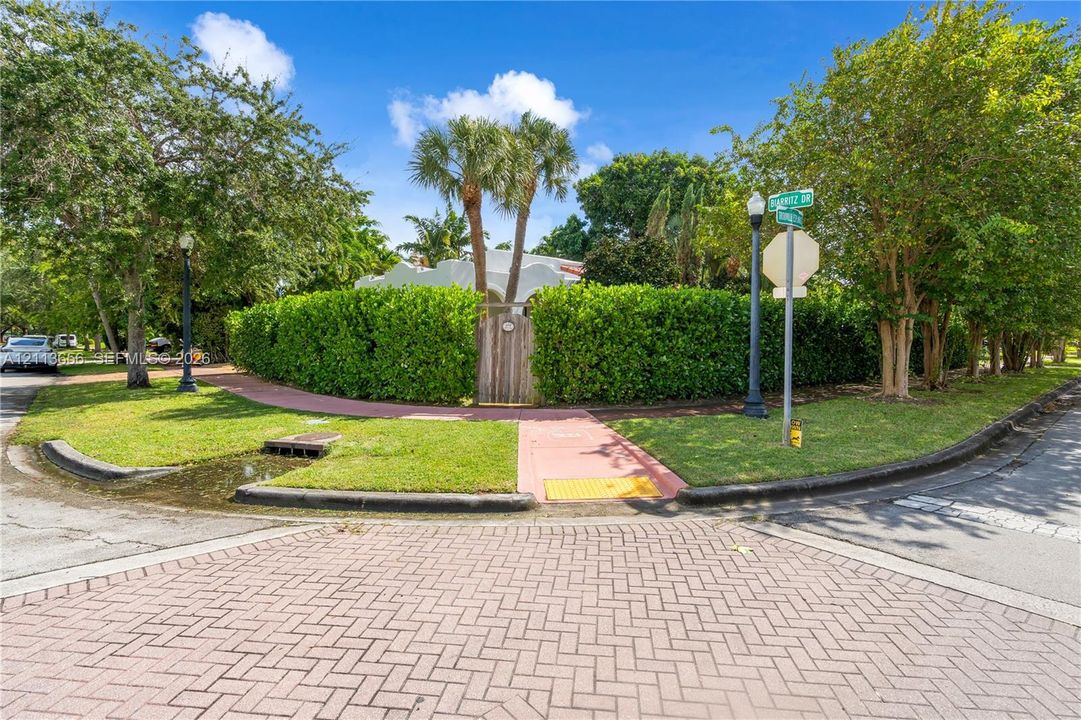 Corner lot property featuring mature landscaping, dense privacy hedging, and palm trees with a gated wood entryway