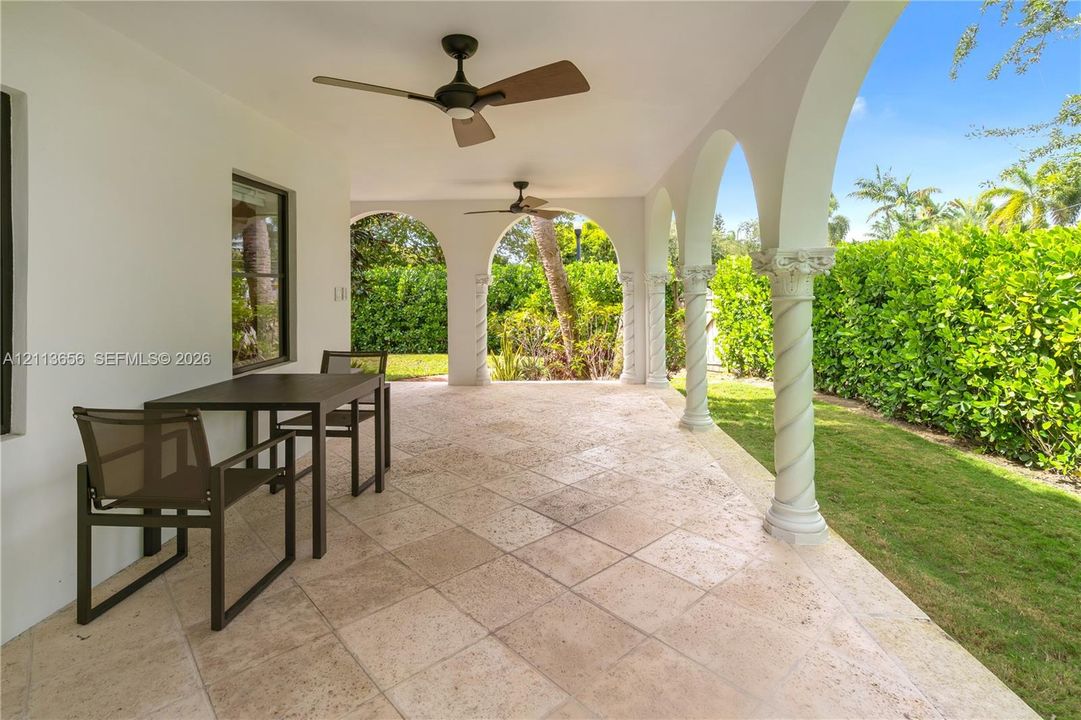Covered patio featuring stone tile flooring, decorative twisted columns with ornate capitals, arched structural openings, and dual ceiling fans