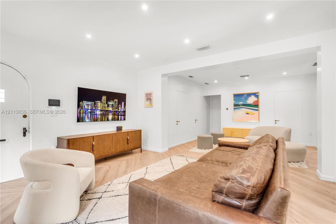 Living area featuring herringbone-pattern wood-finish flooring, recessed lighting, and an arched entry door