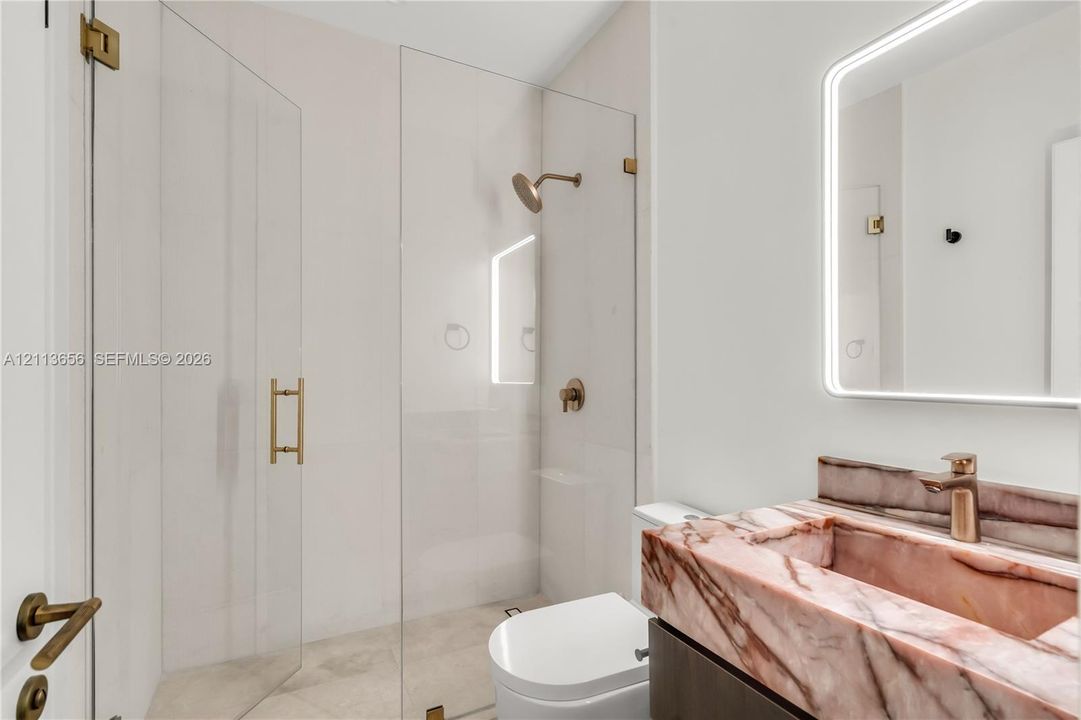 Bathroom featuring a custom integrated stone sink, frameless glass shower enclosure, metallic fixtures, and a backlit vanity mirror