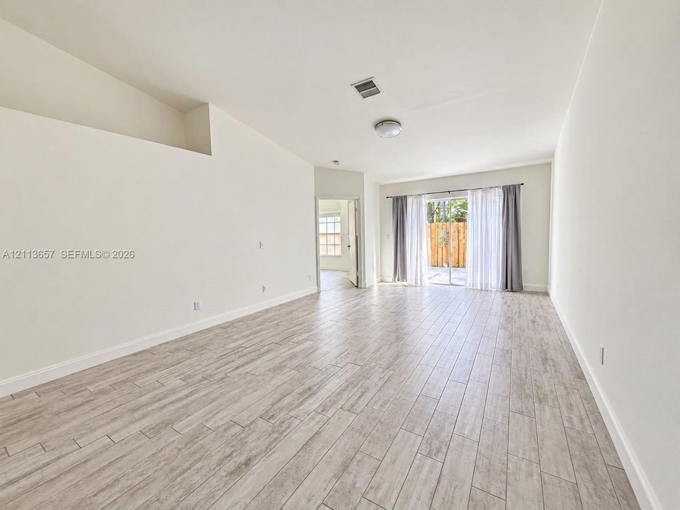 Open-concept room featuring vaulted ceilings, wood-finish tile flooring, and sliding glass doors