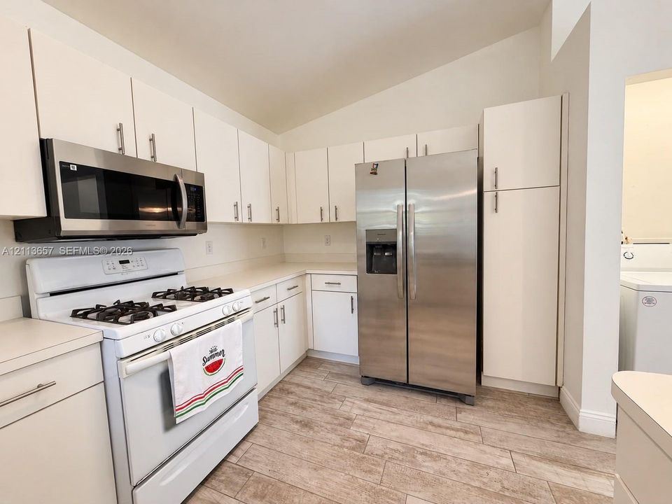 Kitchen featuring white cabinetry, wood-finish flooring, vaulted ceiling, and stainless steel appliances including a built-in microwave and side-by-side refrigerator