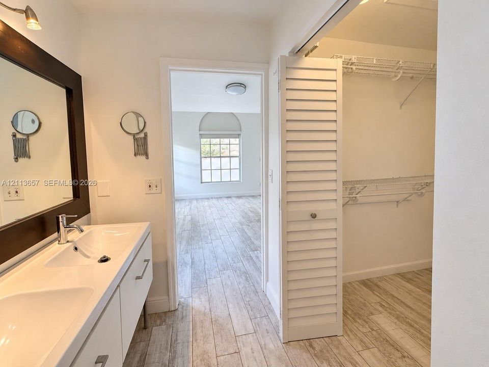 Bathroom vanity with dual integrated sinks, wood-finish tile flooring, and louvered bifold closet doors