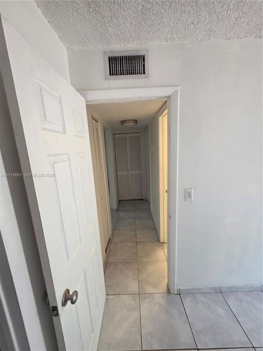 Interior hallway featuring ceramic tile flooring, neutral wall finishes, and multiple sets of louvered closet doors