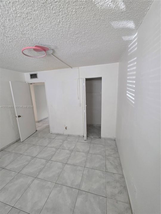 Neutral interior room featuring large-format ceramic tile flooring, textured ceiling, and closet storage with bi-fold doors