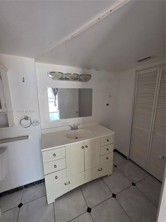 Freestanding vanity with integrated countertop and sink, three-light fixture, rectangular wall-mounted mirror, and tile flooring with decorative inserts