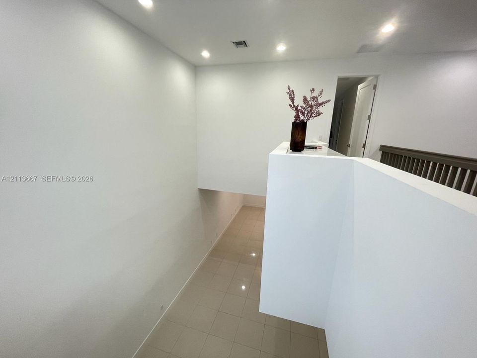 High-ceiling landing featuring tile flooring, recessed lighting, and a painted wooden guardrail