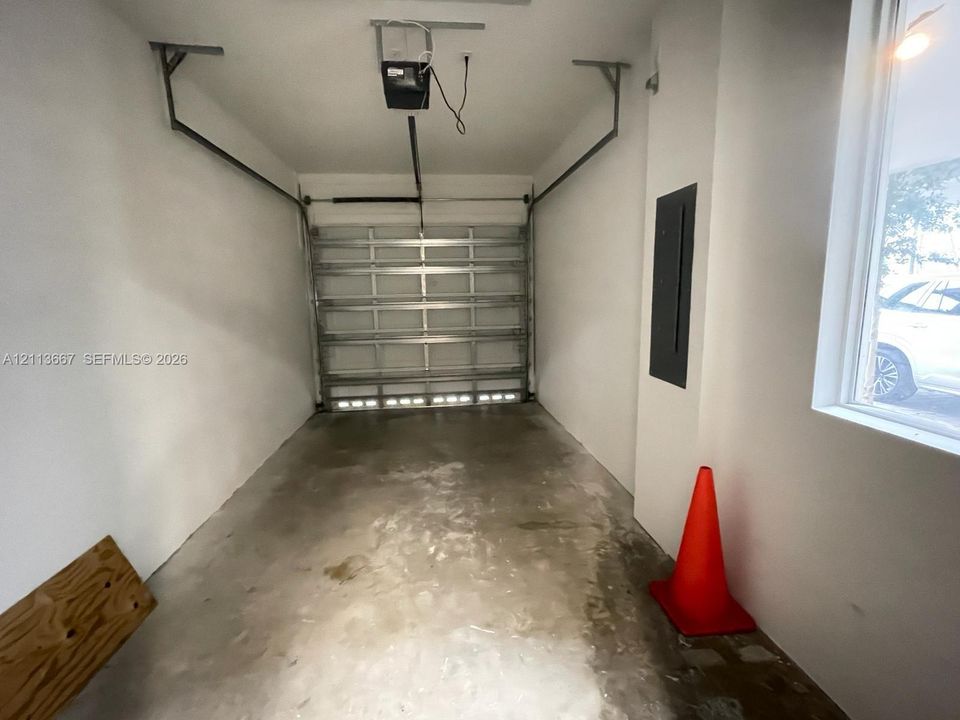 Single-car garage featuring a roll-up metal door, concrete flooring, smooth wall finishes, and an integrated electrical panel