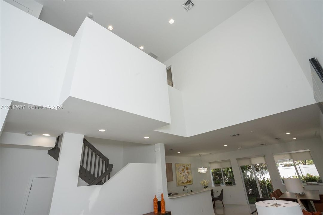 Double-height volume ceiling, recessed lighting, and staircase with dark-toned balustrades