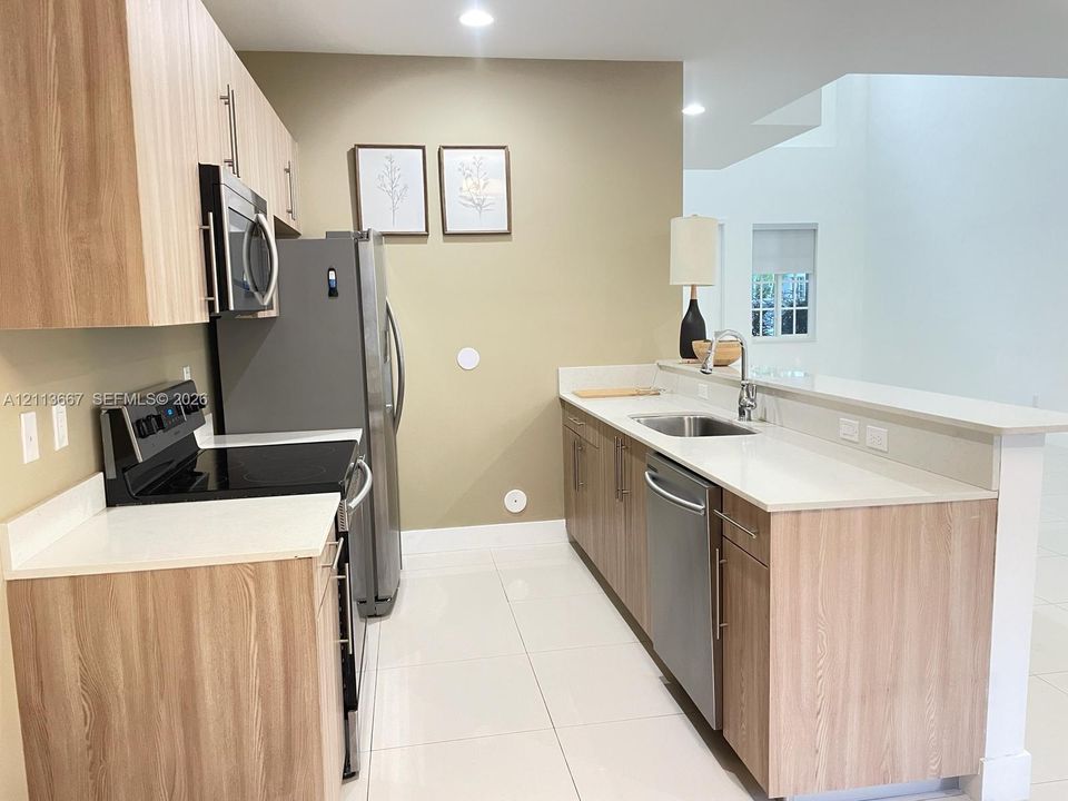 Kitchen featuring light wood-finish cabinetry, white countertops, stainless steel appliances, and tile flooring