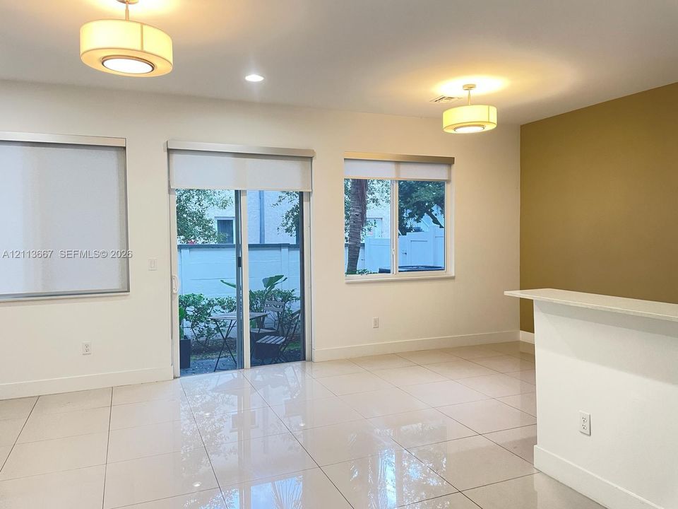 Interior space featuring large-format tile flooring, dual drum pendant lighting, a glass sliding door with integrated window shades, and a built-in counter