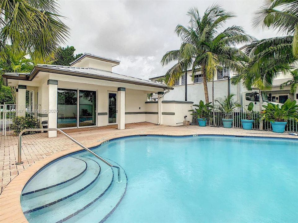 Swimming pool featuring tiered steps, metal handrail, paver pool deck, and perimeter fencing
