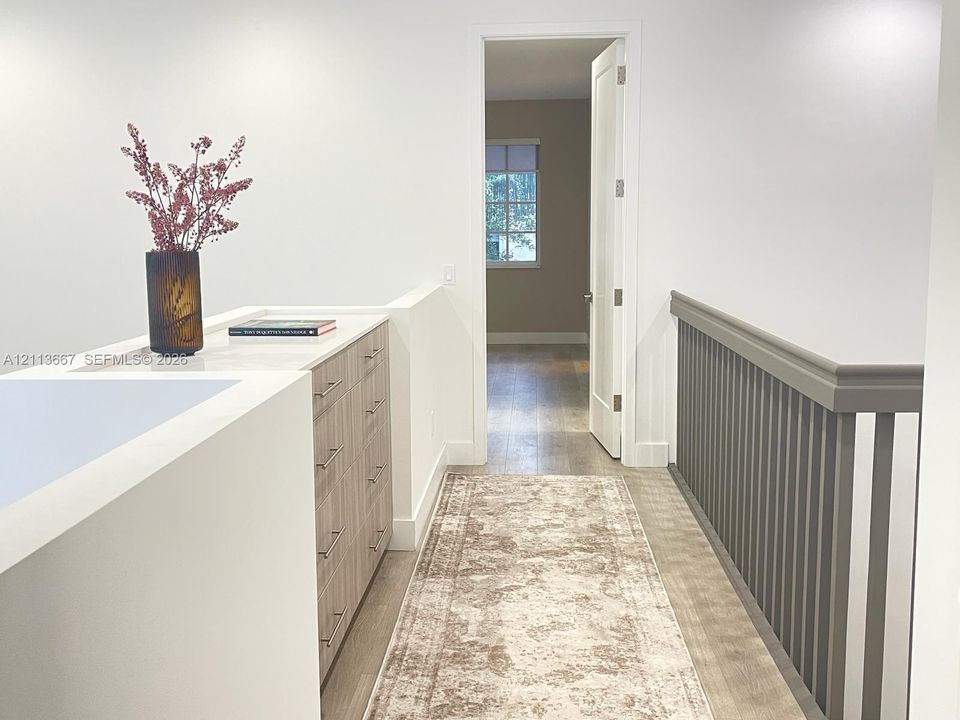Built-in cabinetry featuring light wood-finish drawers, neutral countertop, wood-finish flooring, and painted spindle railing