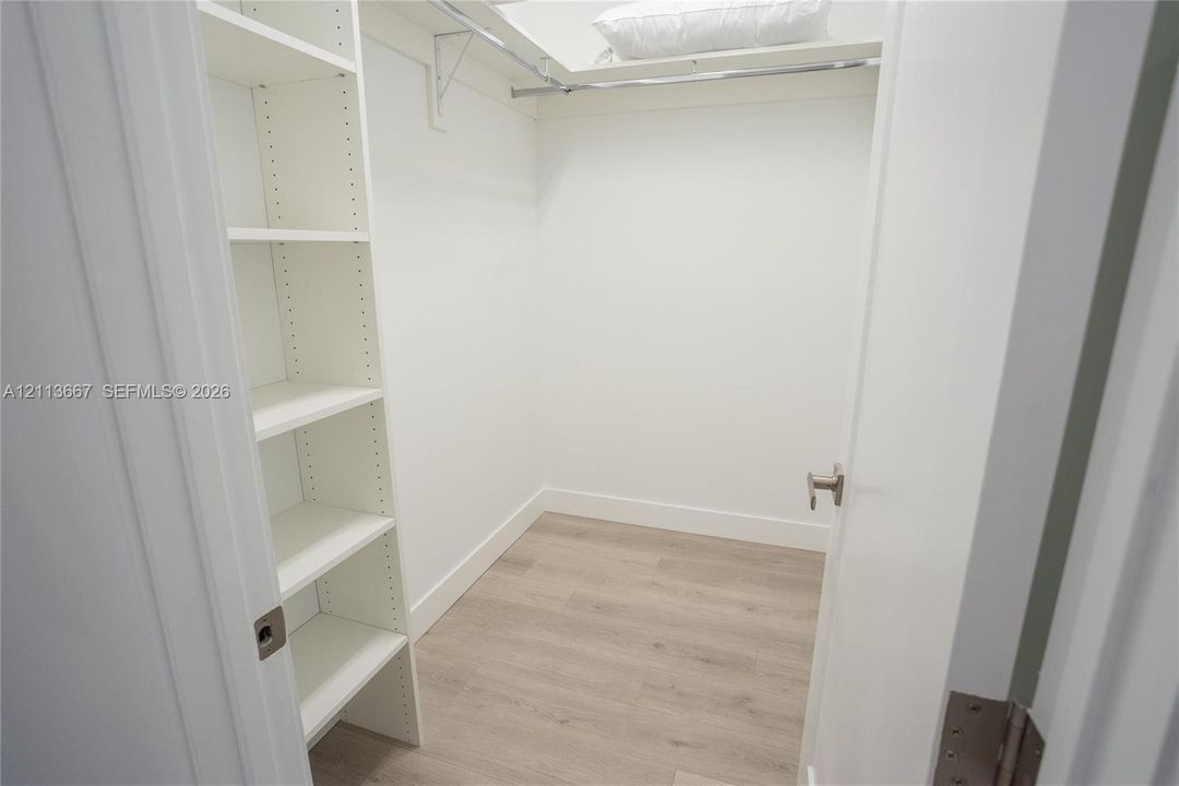 Walk-in closet featuring white built-in shelving, wood-finish flooring, and a metal garment rod