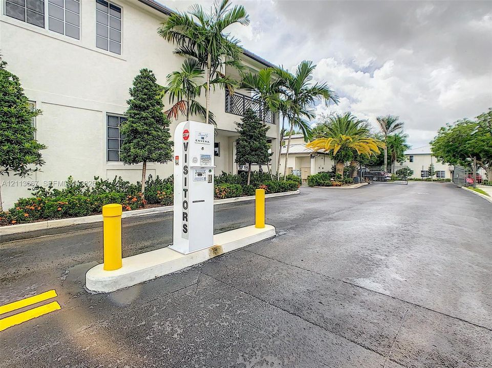 Gated vehicular entrance featuring an electronic access kiosk, asphalt drive, and landscaped grounds