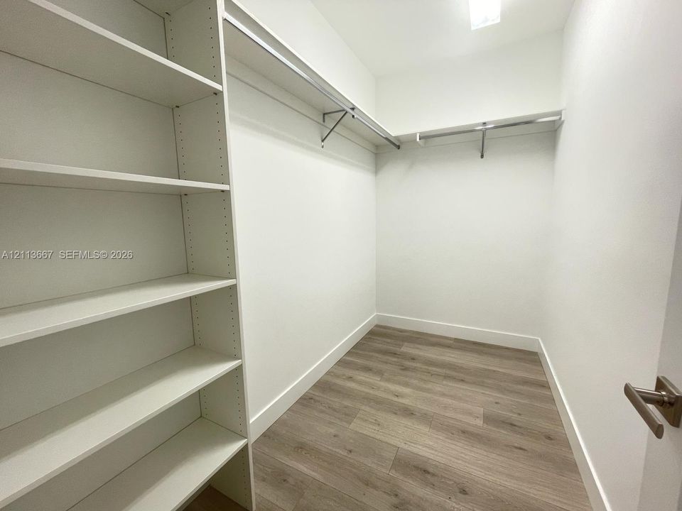 Storage area featuring white built-in shelving, metal garment rods, and wood-finish flooring