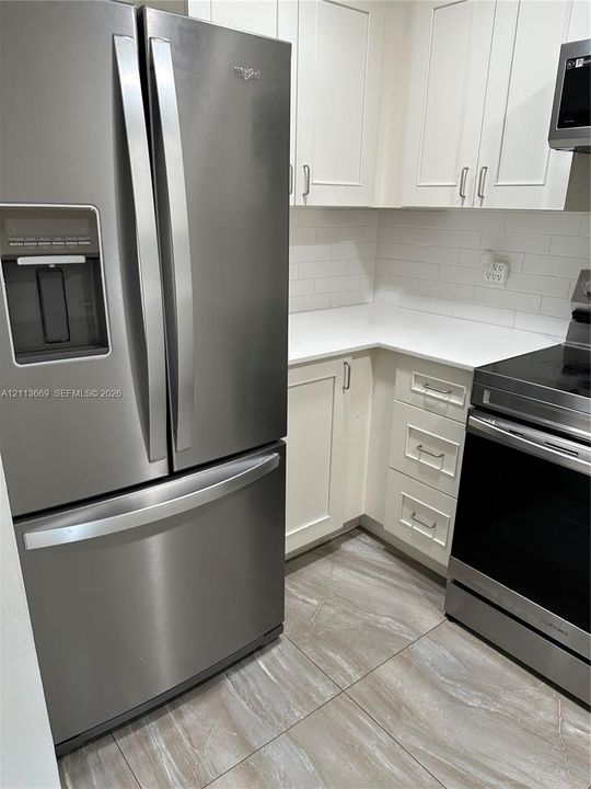 Kitchen featuring stainless steel refrigerator and range, white cabinetry, solid-surface countertops, subway tile backsplash, and ceramic tile flooring