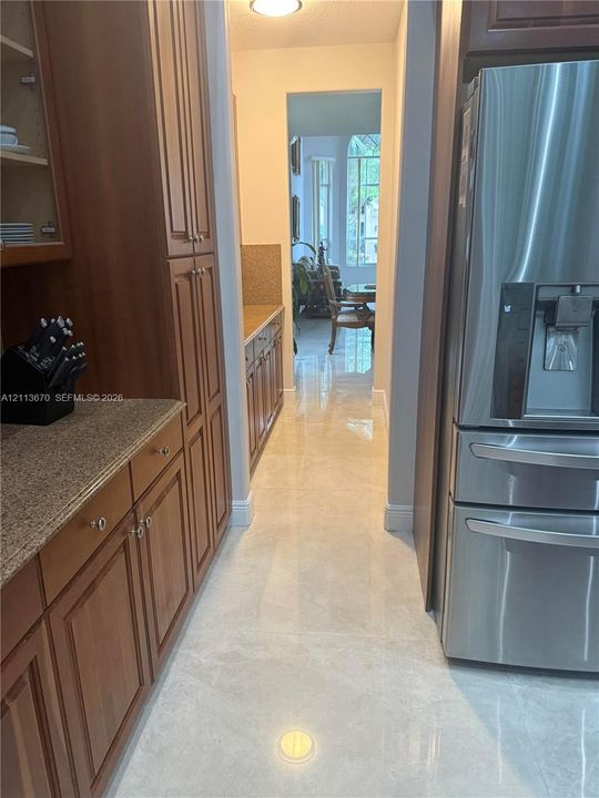 Kitchen featuring custom-built wood cabinetry, stone countertops, large-format tile flooring, and a stainless steel refrigerator