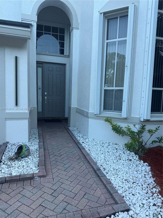 Stucco exterior featuring an arched entryway, herringbone-patterned brick walkway, tall multi-pane windows, and a panelled front door with side light