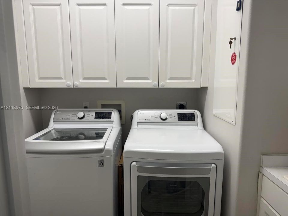 Laundry area featuring white shaker-style overhead cabinetry and built-in washing machine and dryer