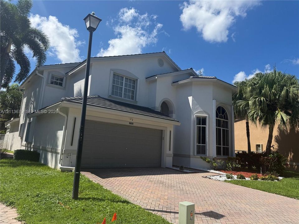 Two-story exterior featuring a light-toned stucco facade, a tile roof, an arched entryway, decorative muntin windows, and a multi-car garage with a paver driveway