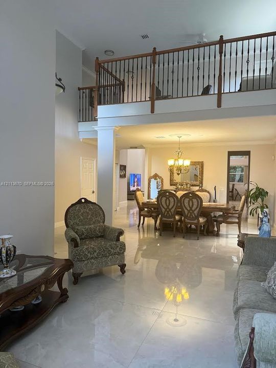 Two-story foyer with high ceilings, polished tile flooring, decorative chandelier, and a balcony featuring wood and metal railings