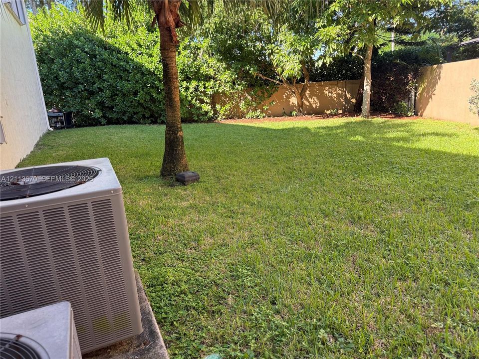 Backyard featuring a grass lawn, mature trees, and perimeter privacy wall