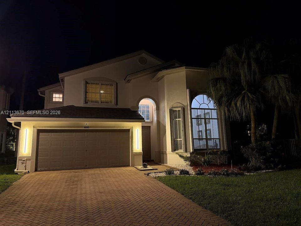 Two-story exterior featuring a paver driveway, an arched entryway, floor-to-ceiling windows with arched transoms, and vertical exterior accent lighting
