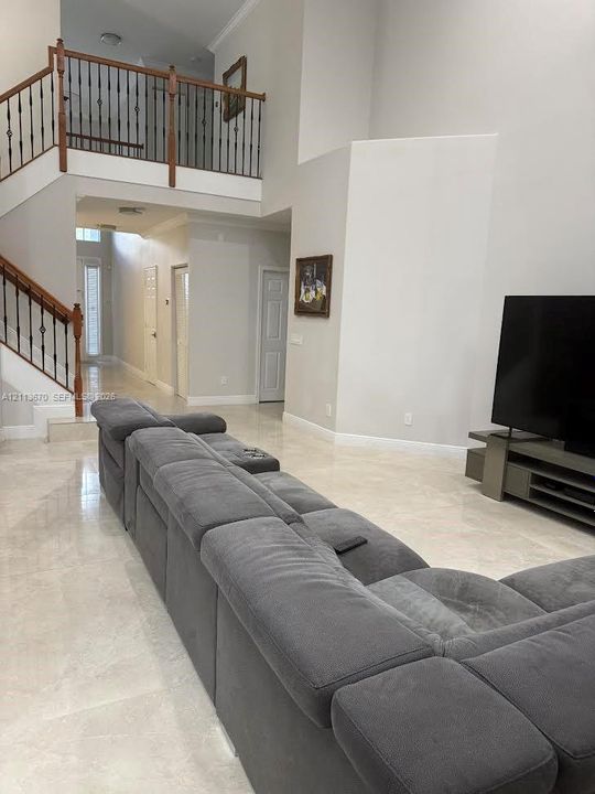 High-ceiling interior featuring a mezzanine overlook, tile flooring, and a staircase with wooden handrails and iron balusters
