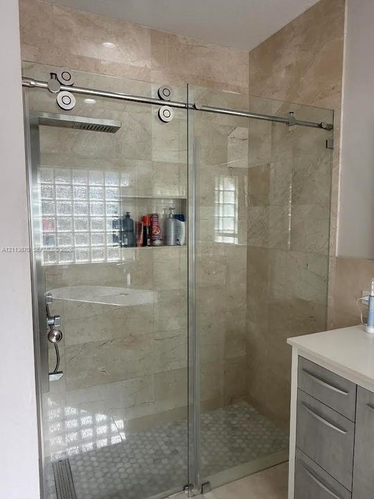 Walk-in shower featuring a sliding glass door with stainless steel hardware, floor-to-ceiling neutral tile, a built-in recessed wall niche, a rain-style showerhead, and a hexagon-tiled shower floor