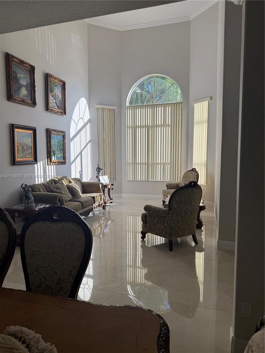 High-ceilinged living area featuring large-format polished tile flooring, an expansive arched window, and neutral wall tones