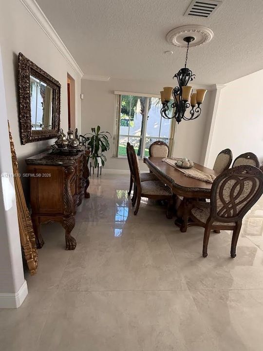 Dining area featuring polished large-format tile flooring, crown molding, a decorative ceiling medallion, and a multi-arm metal chandelier