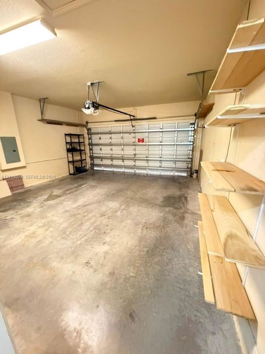 Two-car garage featuring a sectional metal door, concrete flooring, overhead lighting, and built-in wood shelving units
