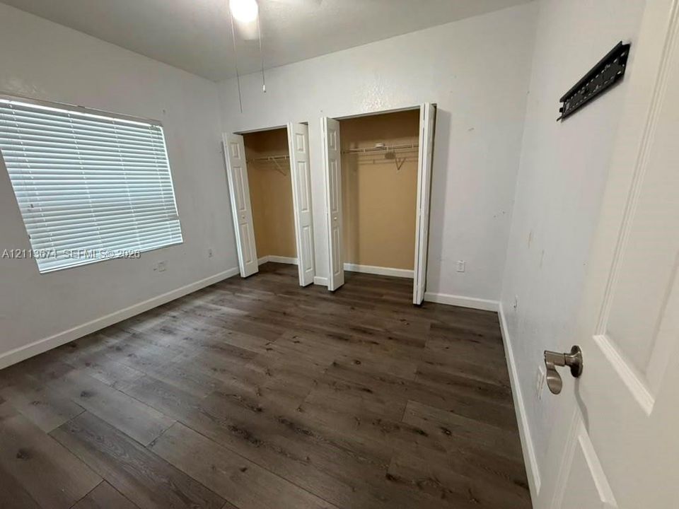 Interior room featuring wood-finish flooring, two closets with bi-fold doors, and a window with horizontal blinds
