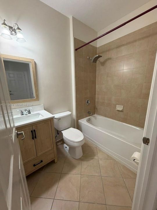 Bathroom featuring a wood-finish vanity with a rectangular sink, square tile flooring, a porcelain tub-and-shower combination with tiled surround, and a framed mirror