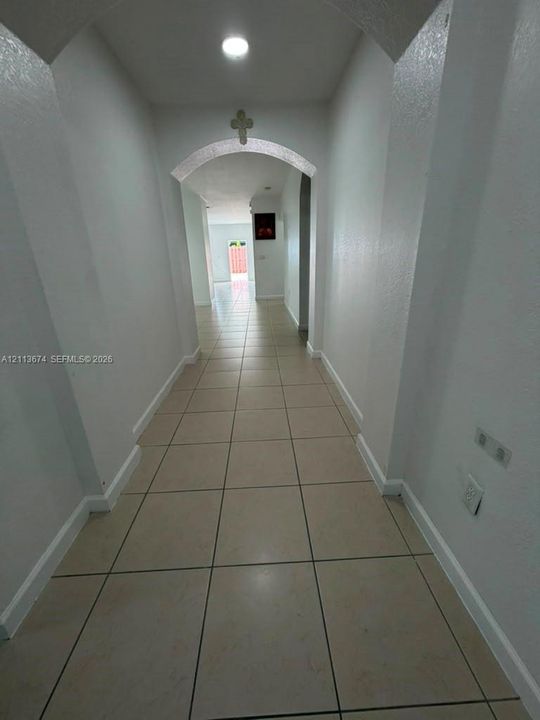 Hallway featuring neutral ceramic tile flooring, architectural arched openings, and recessed ceiling lighting