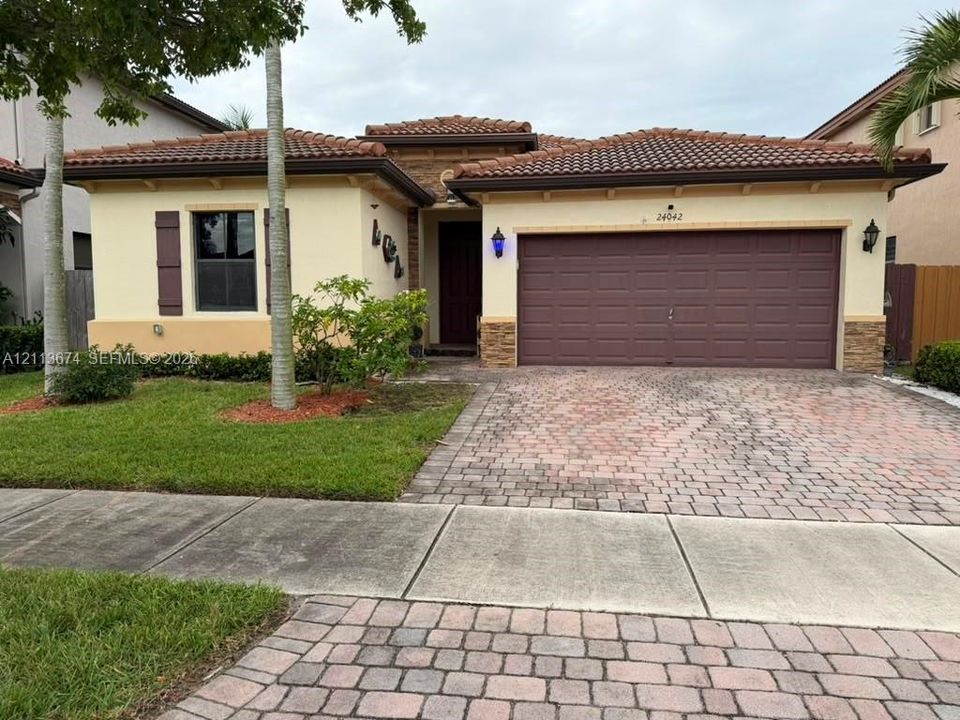 Stucco exterior featuring decorative stone accents, a multi-section tile roof, and a paved stone driveway