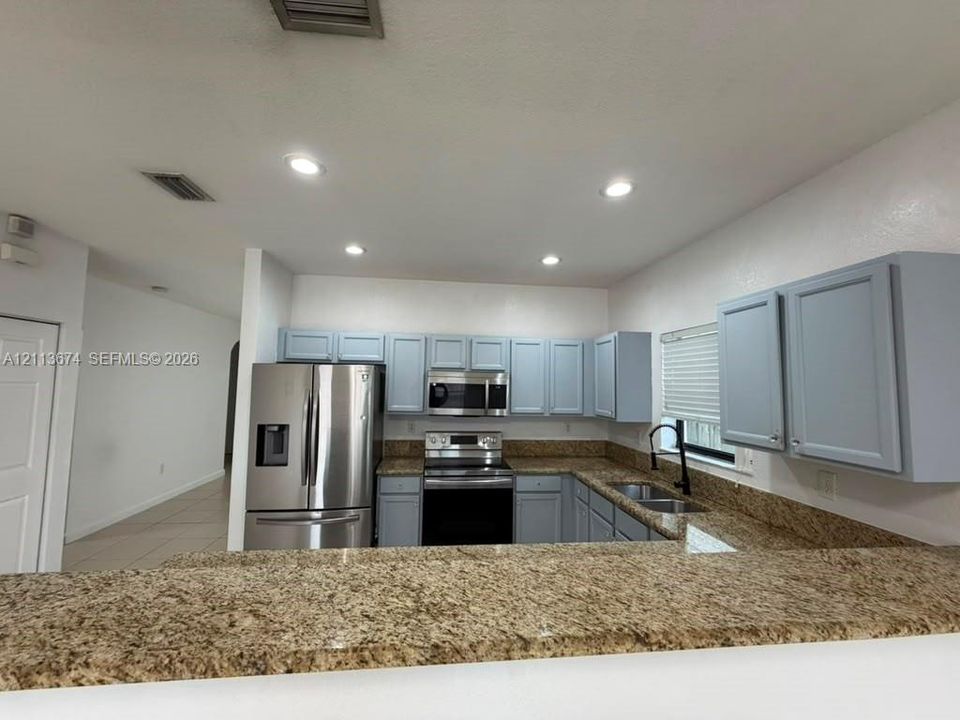 Kitchen featuring light blue cabinetry, stone-surface countertops, stainless steel appliances, dual-basin under-mount sink with matte black faucet, and recessed lighting