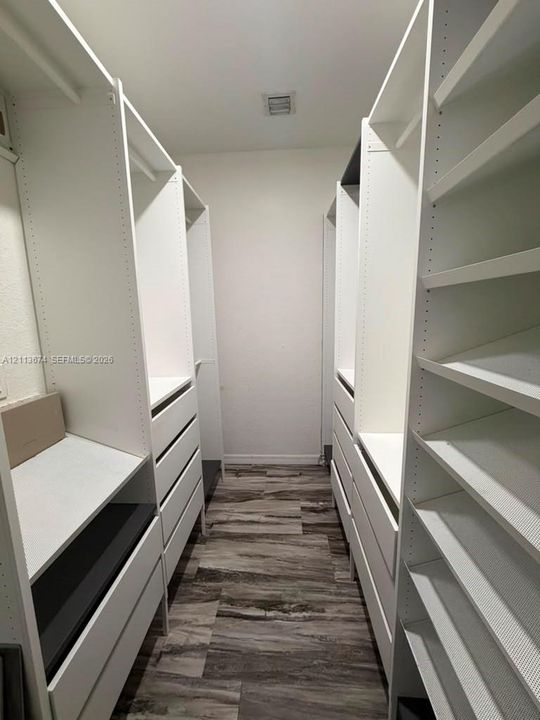 Walk-in closet featuring white built-in shelving, integrated storage drawers, hanging rods, and wood-finish flooring
