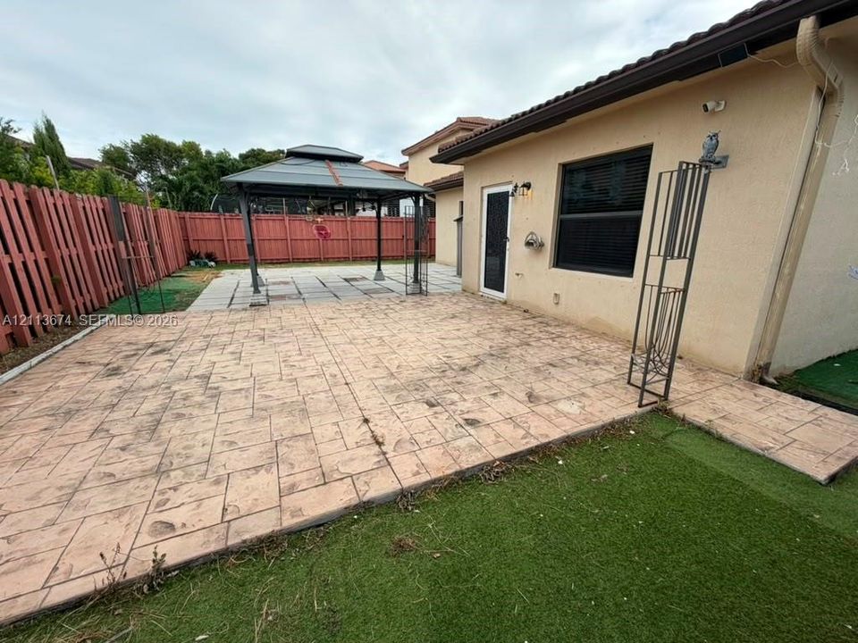 Stamped concrete patio, artificial turf lawn, metal privacy fencing, and metal frame gazebo