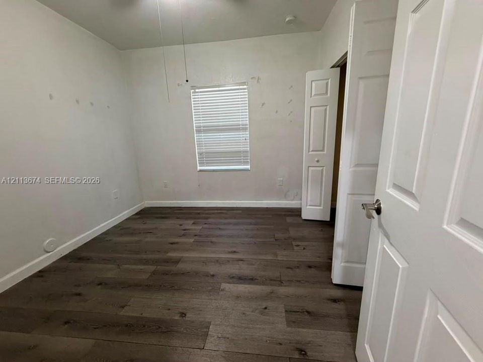Room featuring wood-finish flooring, a single-panel window with horizontal blinds, and two six-panel interior doors with metallic lever handles