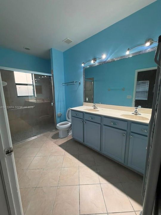 Double vanity with integrated sinks, large wall-mounted mirror, walk-in shower with glass enclosure, and ceramic tile flooring