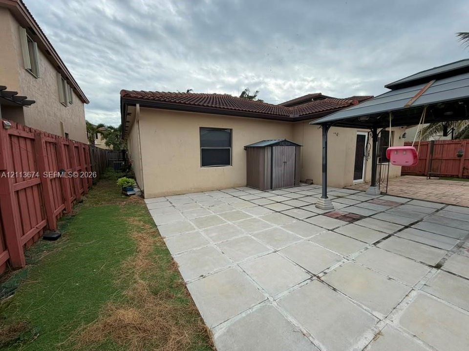 Backyard featuring large-format paver patio, fixed metal gazebo structure, and wood-style perimeter fencing